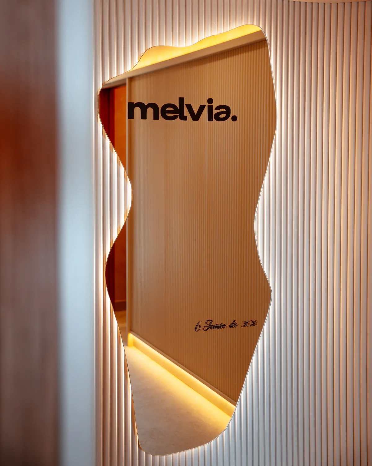 Espejo orgánico de la entrada con el logotipo melvia. y la fecha 6 de junio de 2026 grabada